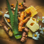 various organic skin care ingredients scattered in a slightly disorganized manner. At the center, there's a fresh turmeric root, with its vibrant golden hue contrasting against the other elements. To its left, a large aloe vera leaf stands tall, exuding a sense of freshness. Surrounding these key ingredients, an assortment of other natural elements are present, such as beeswax, shea butter, and chamomile flowers. The overall composition has an earthy tone, with warm and cool hues, reflecting the blend of organic and natural elements.