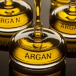 an image showcasing the golden luxurious texture of argan oil, with droplets glistening on three sleek glass bottles. the bottles are labelled 'argan’