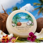 A delightful image of a coconut-scented soap, surrounded by fresh coconut shells and frangrant tropical flowers. The soap has a light, creamy color and is adorned with a beach scene design. In the background, there's a blue sky with fluffy white clouds and palm trees swaying gently in the breeze. The overall feel of the image is warm, inviting, and reminiscent of a sunny beach getaway.