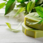 A serene and calming image of a handcrafted green tea soap, with the soap's scent subtly wafting from it. The soap has a beautiful, natural shade of green, adorned with delicate swirls that resemble the leaves of the tea plant. The background is a clean, white surface that highlights the soap's vibrant color and intricate design. The overall ambiance of the photo is peaceful and refreshing, invoking a sense of tranquility and relaxation.